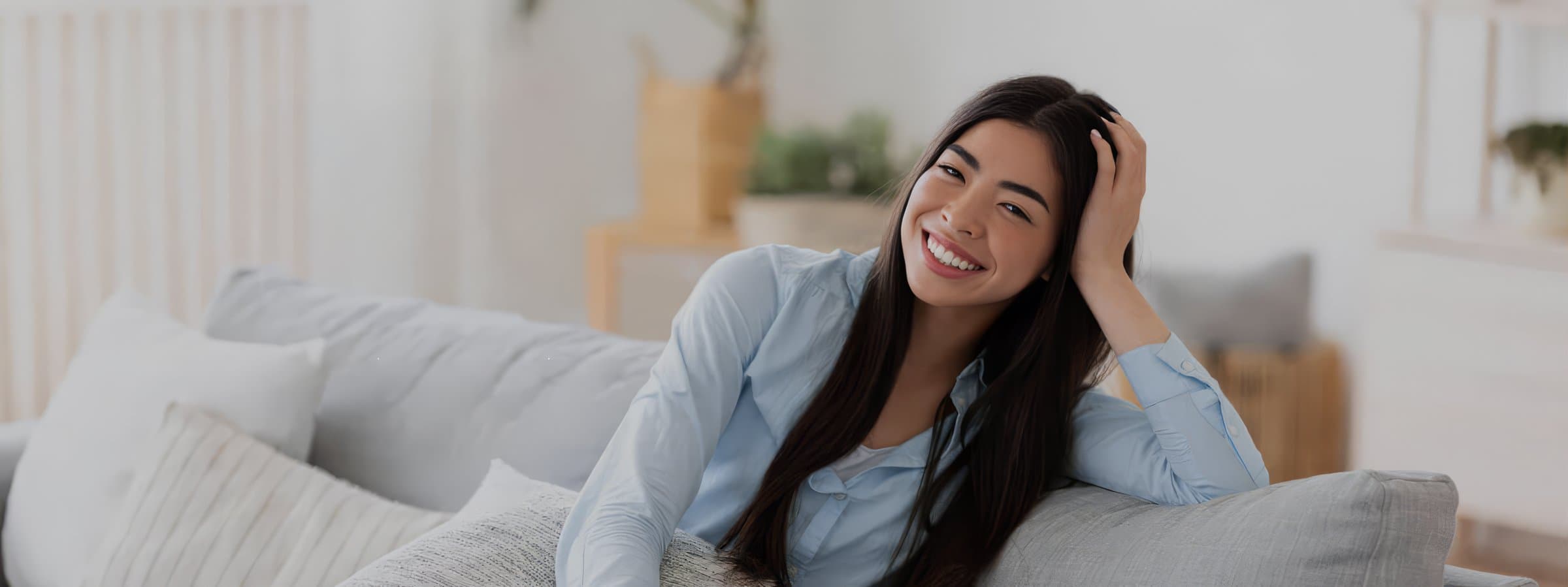 Smiling woman in a light blue shirt seated on a gray couch